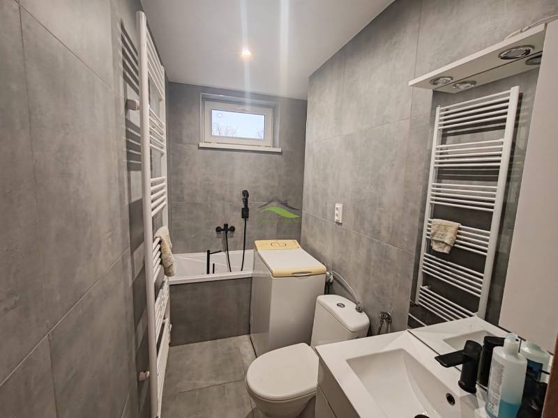 Bathroom in a 3-room apartment with a bathtub, sink, and washing machine, gray tiles.