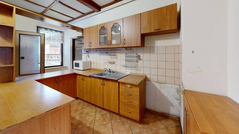 A kitchen in a family house with wooden cabinets, a tiled wall, and ceramic flooring.