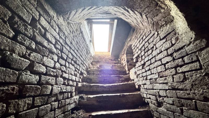 Stone stairs in the basement of a family house with a vaulted ceiling and a light opening.
