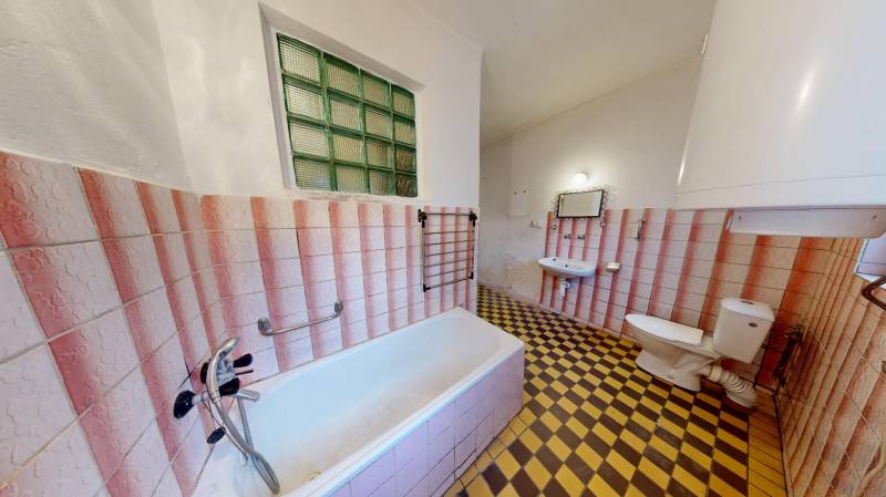 A bathroom in a family house with a bathtub, a sink, and checkered tile flooring.