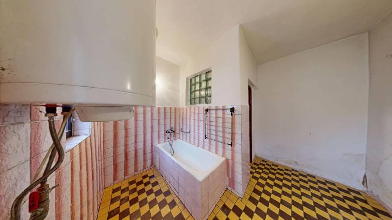 A bathroom in a family house with a bathtub, tiles, and checkered flooring.
