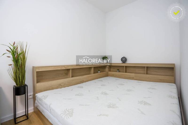 Bedroom in a studio apartment with a bed and wooden decor on the shelf.
