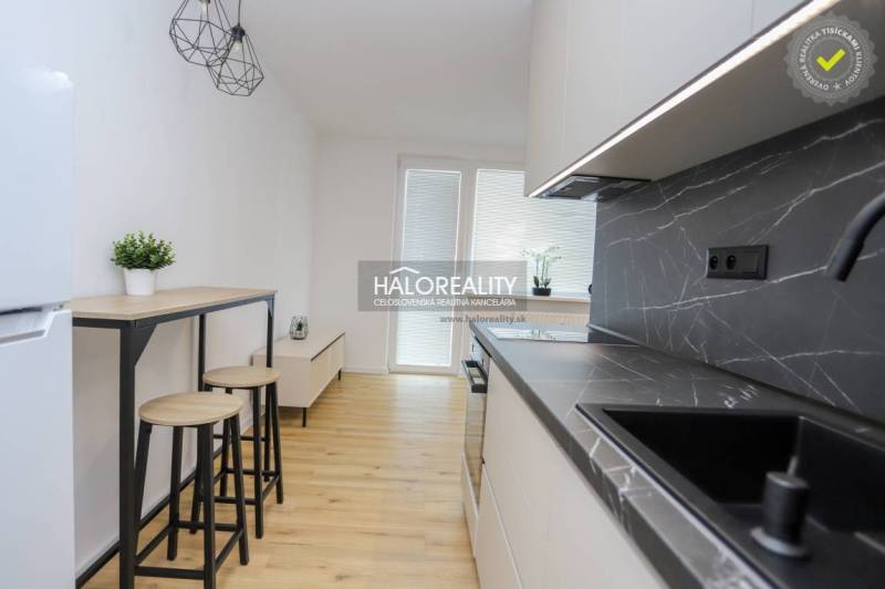 A kitchen in a studio apartment with a black countertop and a wooden decor floor.