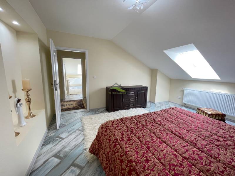 Attic bedroom with a bed, wooden decor flooring, and a skylight in a family house.