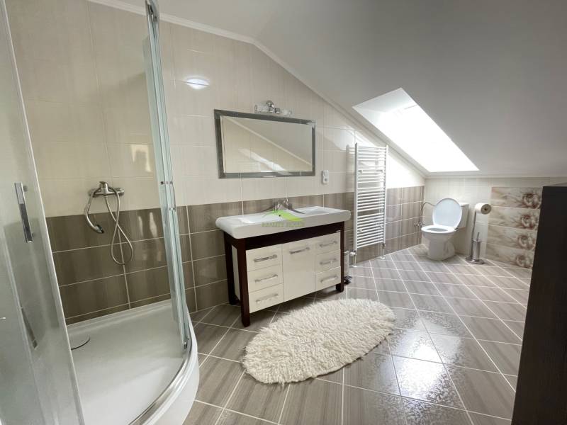 A bathroom in a family house with a large mirror, a shower corner, and tiles.
