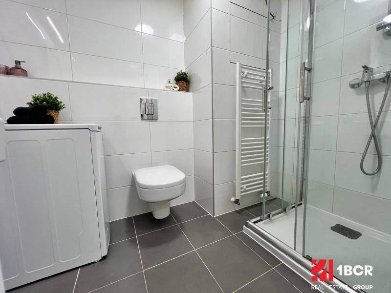 Bathroom with a washing machine, shower corner, and wall-hung toilet in a studio apartment.