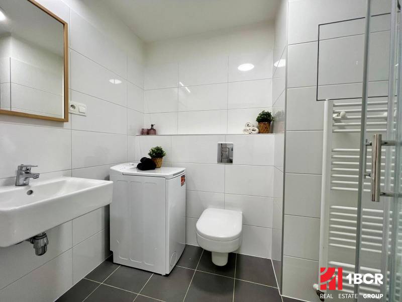 A bathroom with a washing machine and a sink in a studio apartment, with white tiles.