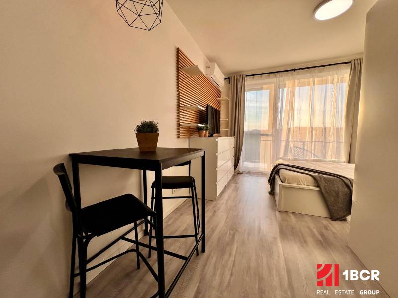 Interior of a 1-room apartment with a wooden decor floor, table, and bed.
