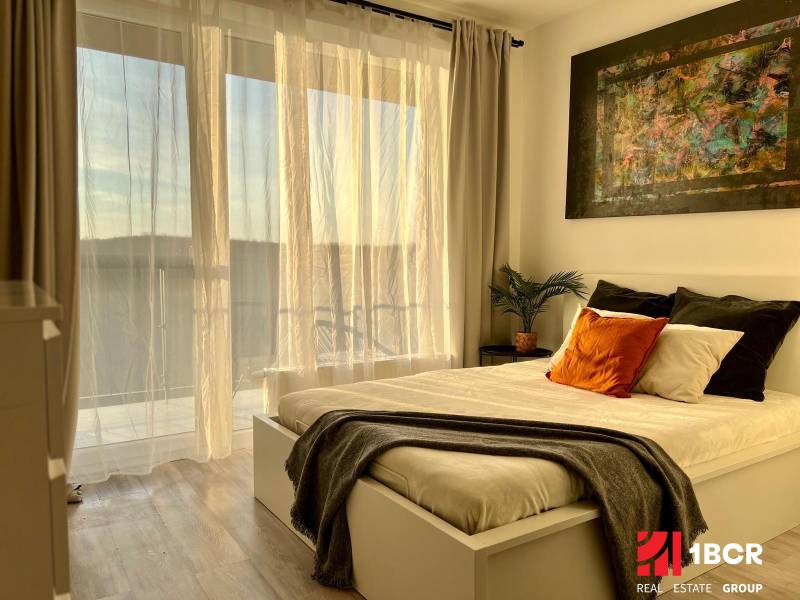 Bedroom with a bed, painting, and curtains in a studio apartment with wood-patterned flooring.