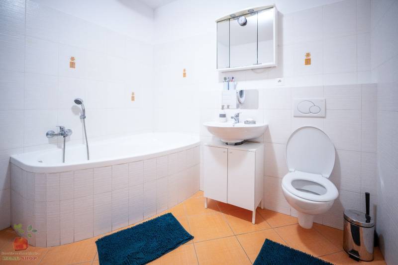 Bathroom with a bathtub in a 3-room apartment; white tiles, orange floor tiles, blue rugs.