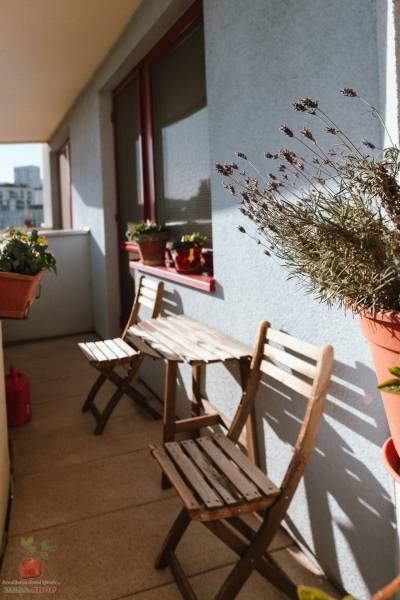 A balcony in a 3-room apartment with wooden seating and flowers on the edge.