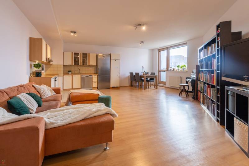 Living room in a three-room apartment with a wood-decor floor, corner kitchen, and dining table.