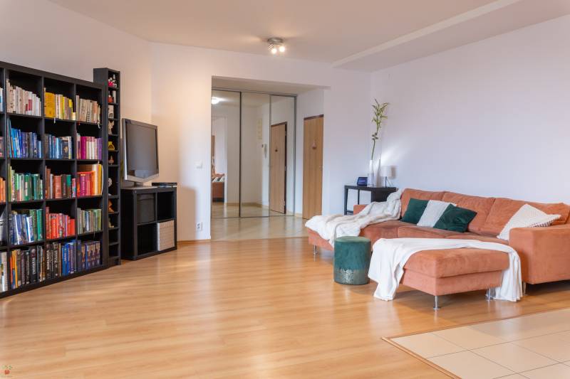 Living room of a 3-room apartment with a wooden decor floor, a shelf, and a comfortable orange sofa.