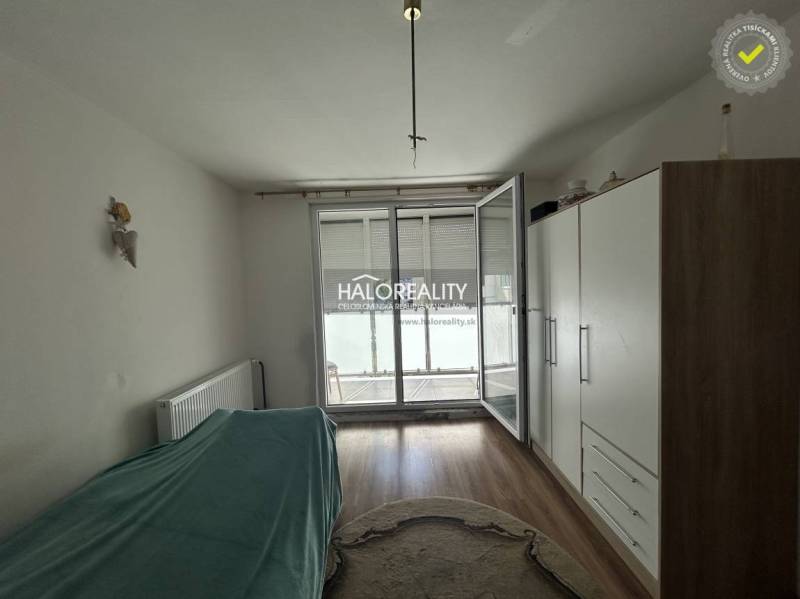 A room in a 2-room apartment with a wooden decor floor, a large wardrobe, and balcony doors.