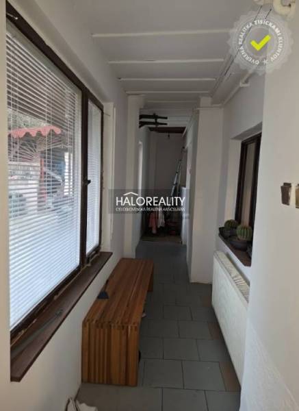 A narrow hallway in a family house with flowers, a wooden bench, and large windows.