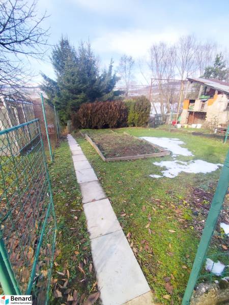 Garden plots in Malý Slivník with a walkway and vegetation, surrounded by a fence.