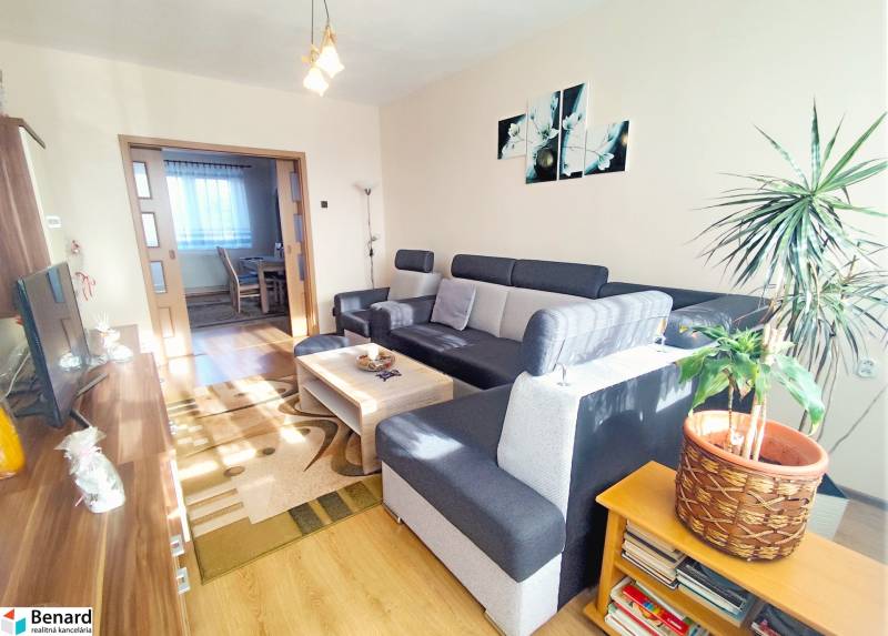 Living room with wood-patterned flooring and a gray sofa in a three-room apartment.