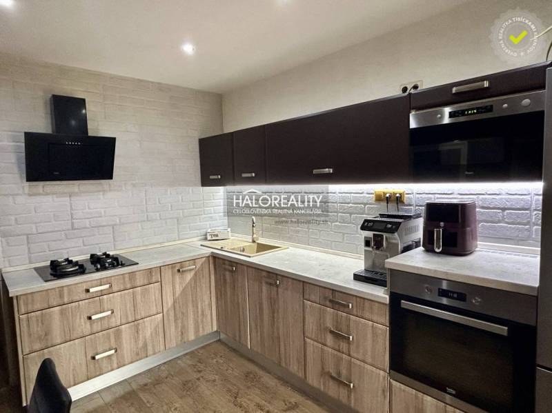 A kitchen in a 3-room apartment with a wooden decor and a white brick wall cladding.