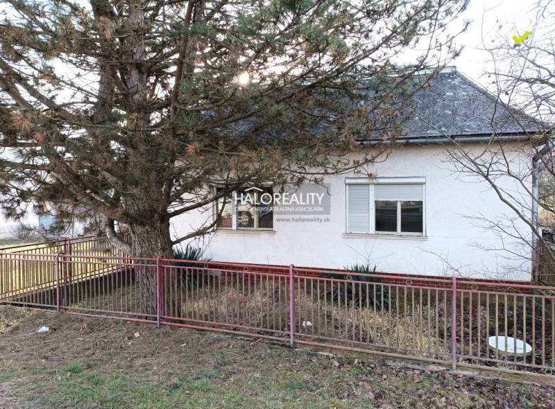 A family house with a white facade, a tree in the garden, and a red fence.
