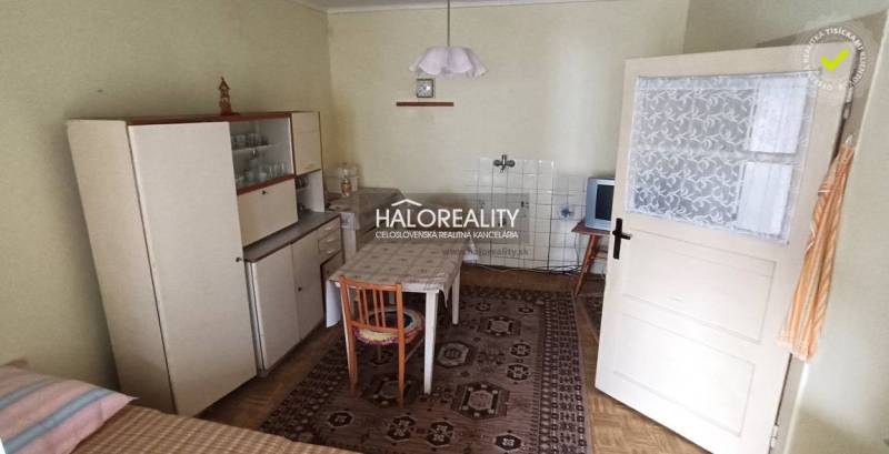 Rustic kitchen with a wooden cabinet, dining table, and television in a family house.