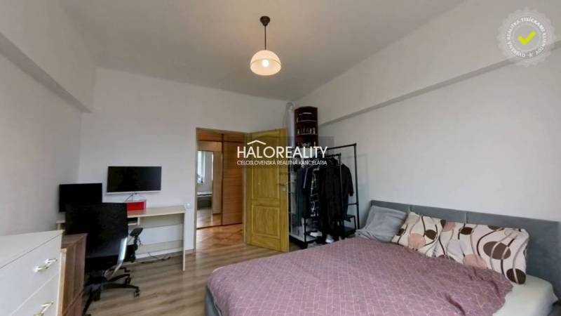 Bedroom in a 2-room apartment with a bed, a desk, and a wooden decor floor.