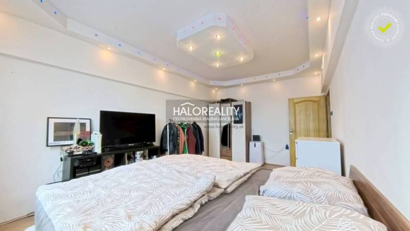 A room in a 2-room apartment with a bed, TV, and minimalist lighting.