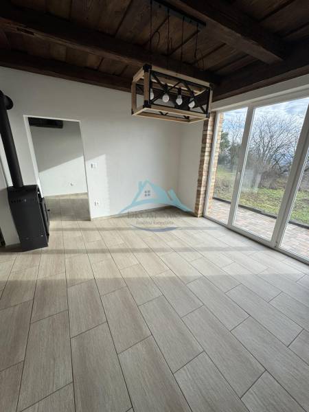 The interior of a cabin with a light wood-patterned floor, a fireplace, and large windows.