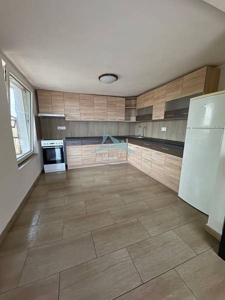 A kitchen in a cottage with light furniture, a wooden decor floor, and a large window.