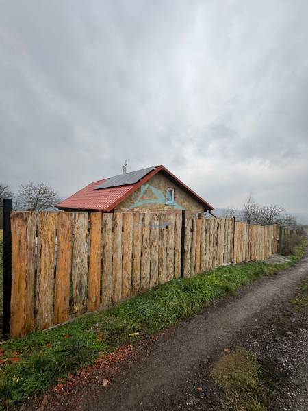 A cottage in Šahy with a red roof and a wooden fence by a country road.