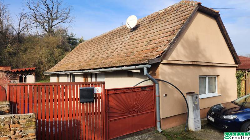 A family house in Brestovany with a red gate and roof, surrounded by greenery and a car.