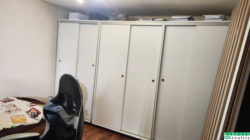A room in a family house with white cabinets, a gaming chair, and a wooden decor floor.