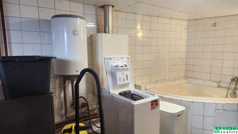 A bathroom in a family house with a washing machine, boiler, and a tiled bathtub.