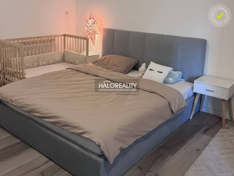 A bedroom in a 4-room apartment with a large bed, a baby crib, and a floor with a wooden decor.