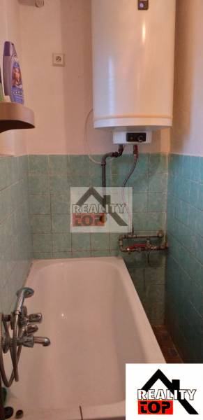 A bathroom with green tiles, a bathtub, and a boiler in a family house.