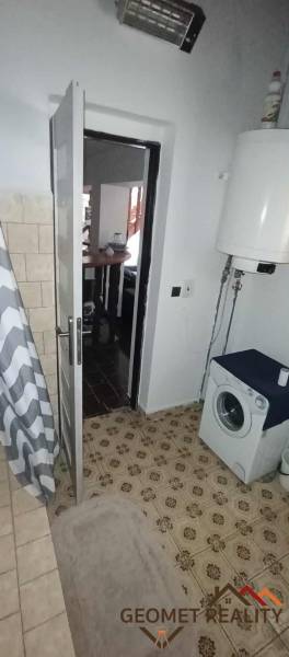 A bathroom in a cottage with a washing machine, shower curtain, and water heater.