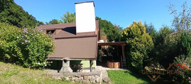 A cottage in Ružiná surrounded by greenery, outdoor seating, and a stone fireplace.