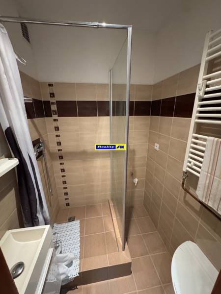 A bathroom of a two-room apartment with a shower and beige tiles.
