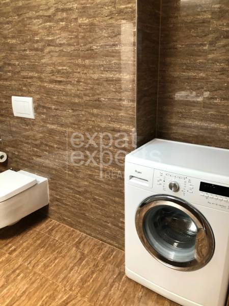 A bathroom with a wooden decor floor and a washing machine in a 2-room apartment.