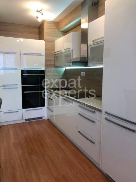 A kitchen in a 2-room apartment with glossy white cabinets and a floor with a wood decor.