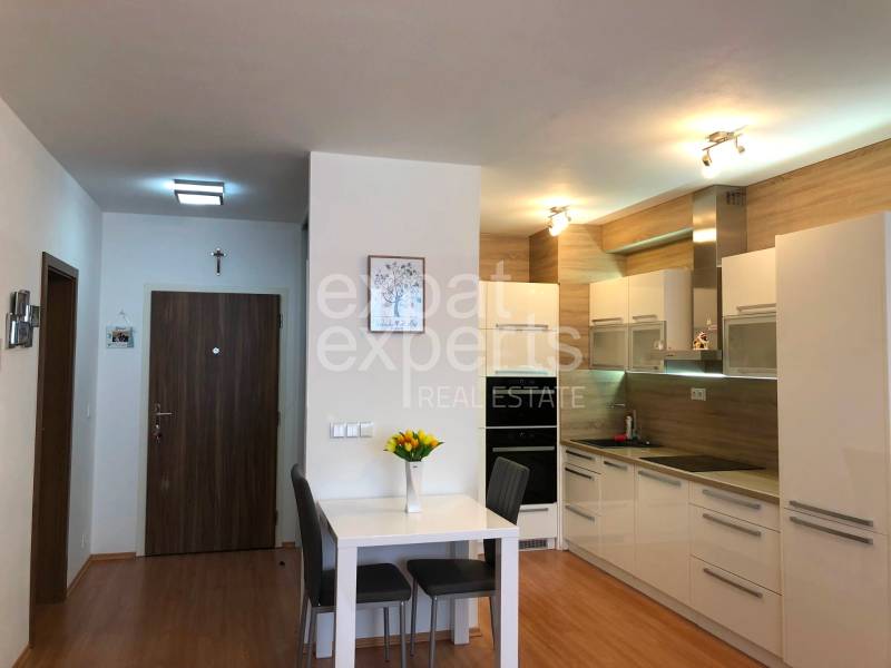 A kitchen with white furniture and a dining table in a 2-room apartment, flooring with a wooden decor.