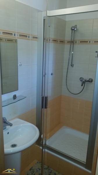 Bathroom in a holiday apartment with a sink, shower, and mirror with a shelf.