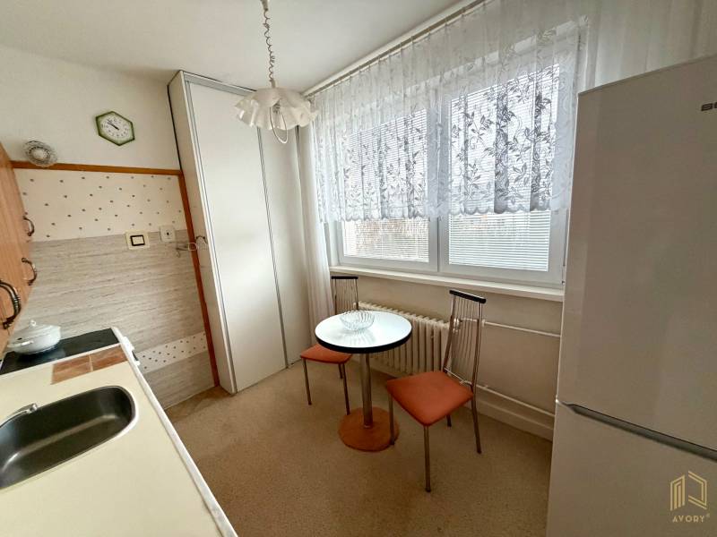 A kitchen in a 3-room apartment with a dining table, chairs, and a refrigerator.