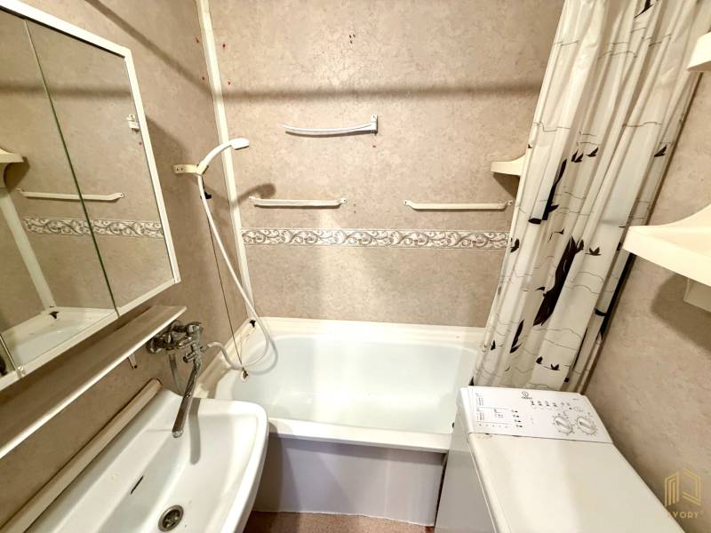 A bathroom in a 3-room apartment with a classic bathtub, shower head, and washing machine.