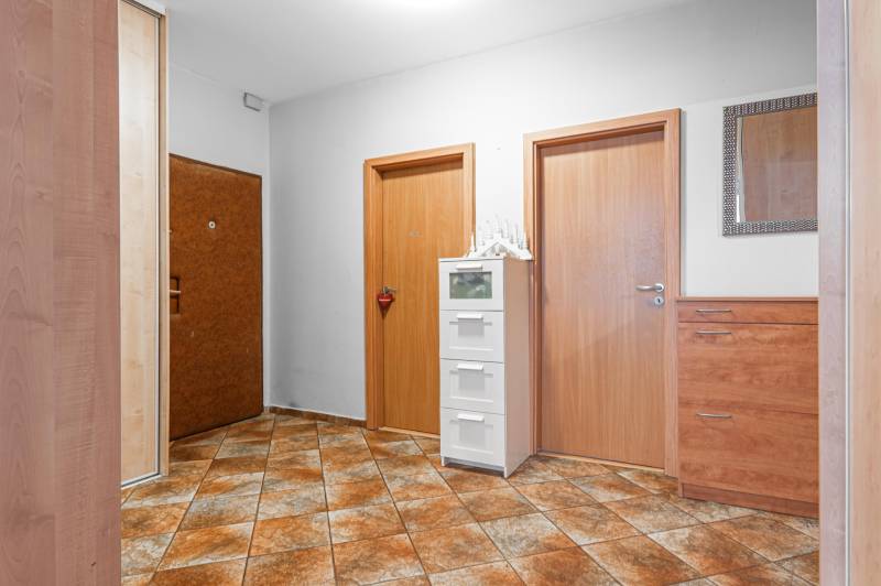 Hallway in a 4-room apartment with tiles, wooden doors, and storage furniture.