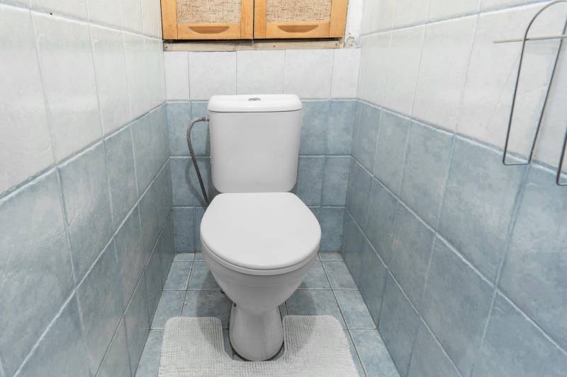 A bathroom in a 4-room apartment with blue tiles, a white toilet, and a cabinet above it.