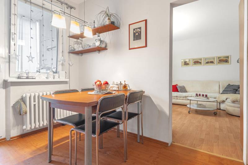 Dining area with a wooden table, shelves, and a view of the living room in a 4-room apartment.