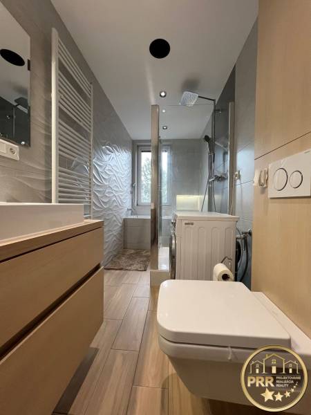 Bathroom in a 3-room apartment with a sink, shower, and washing machine, floor with wood decor.