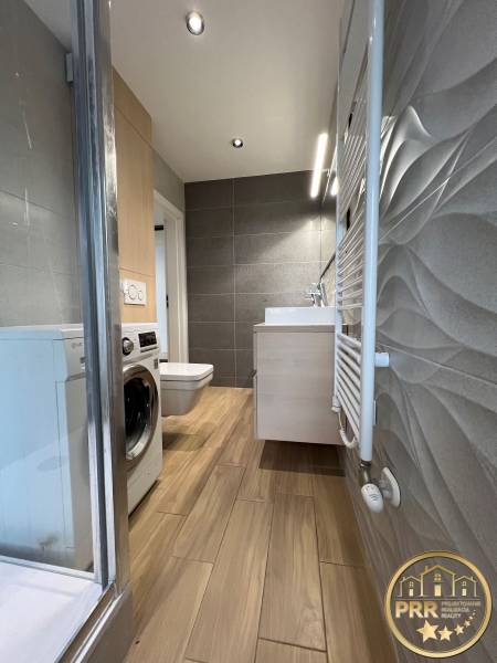 A bathroom in a 3-room apartment with a washing machine, shower, and a floor with a wooden decor.