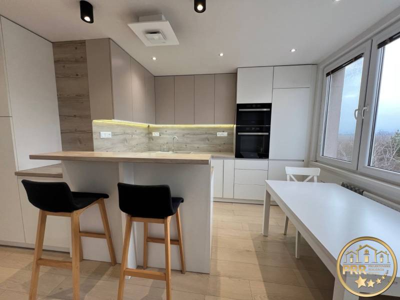 A kitchen in a 3-room apartment with light furniture and a wooden decor floor.