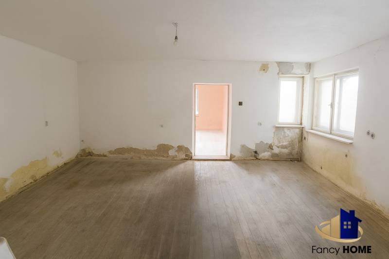 A room in a family house with a wooden decor floor and damaged walls.
